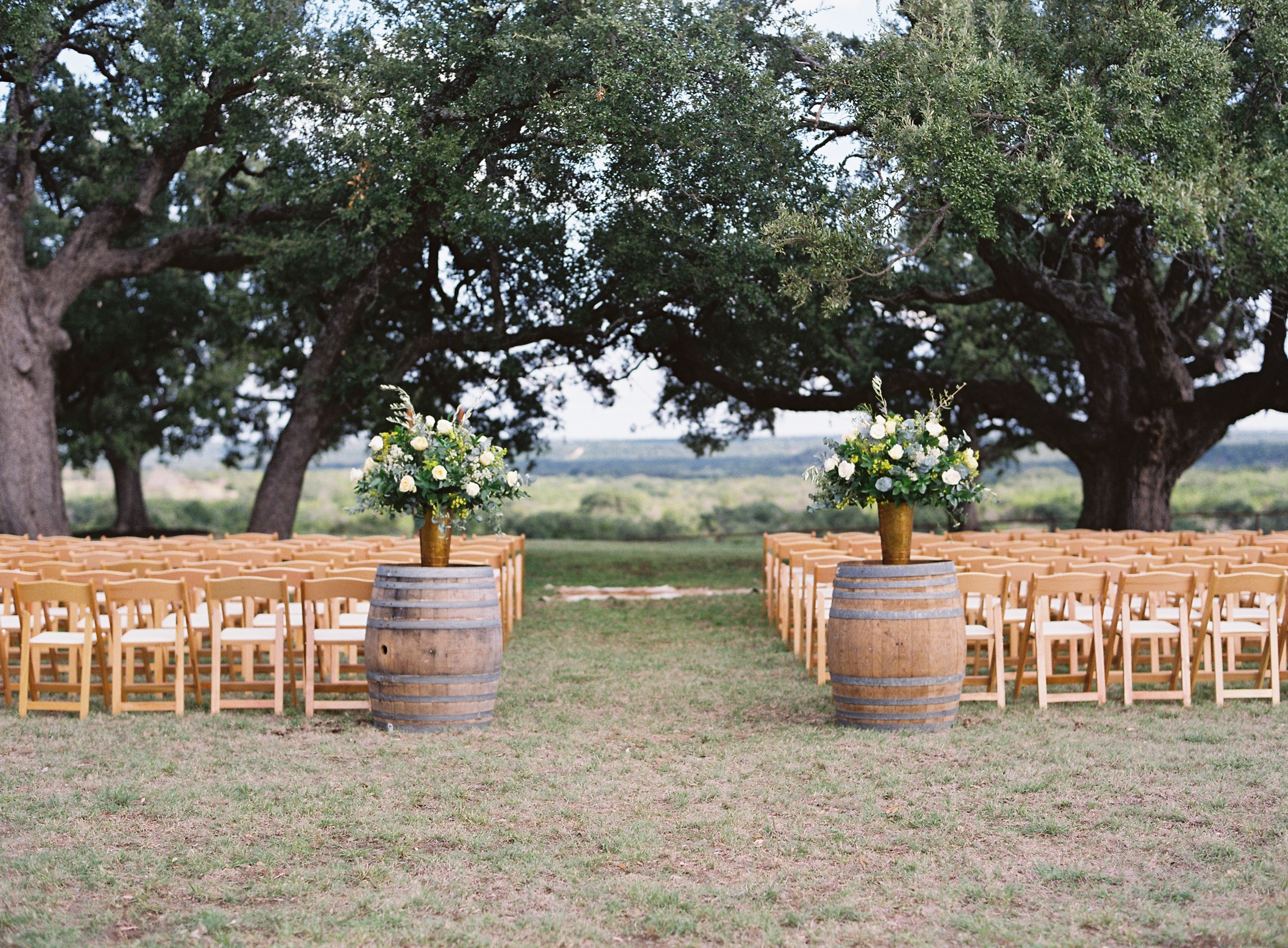 Outdoor Texas wedding venue with ceremony chairs and floral arrangements on whiskey barrels.