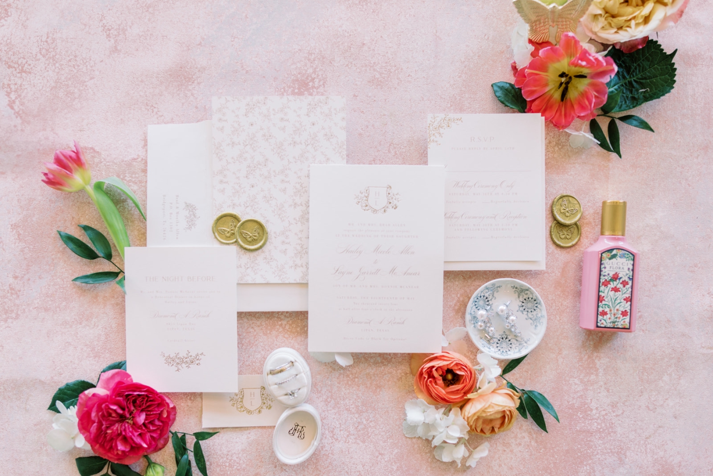 A flat-lay of wedding invitations, rings, and flowers for a May wedding at Diamond A Ranch