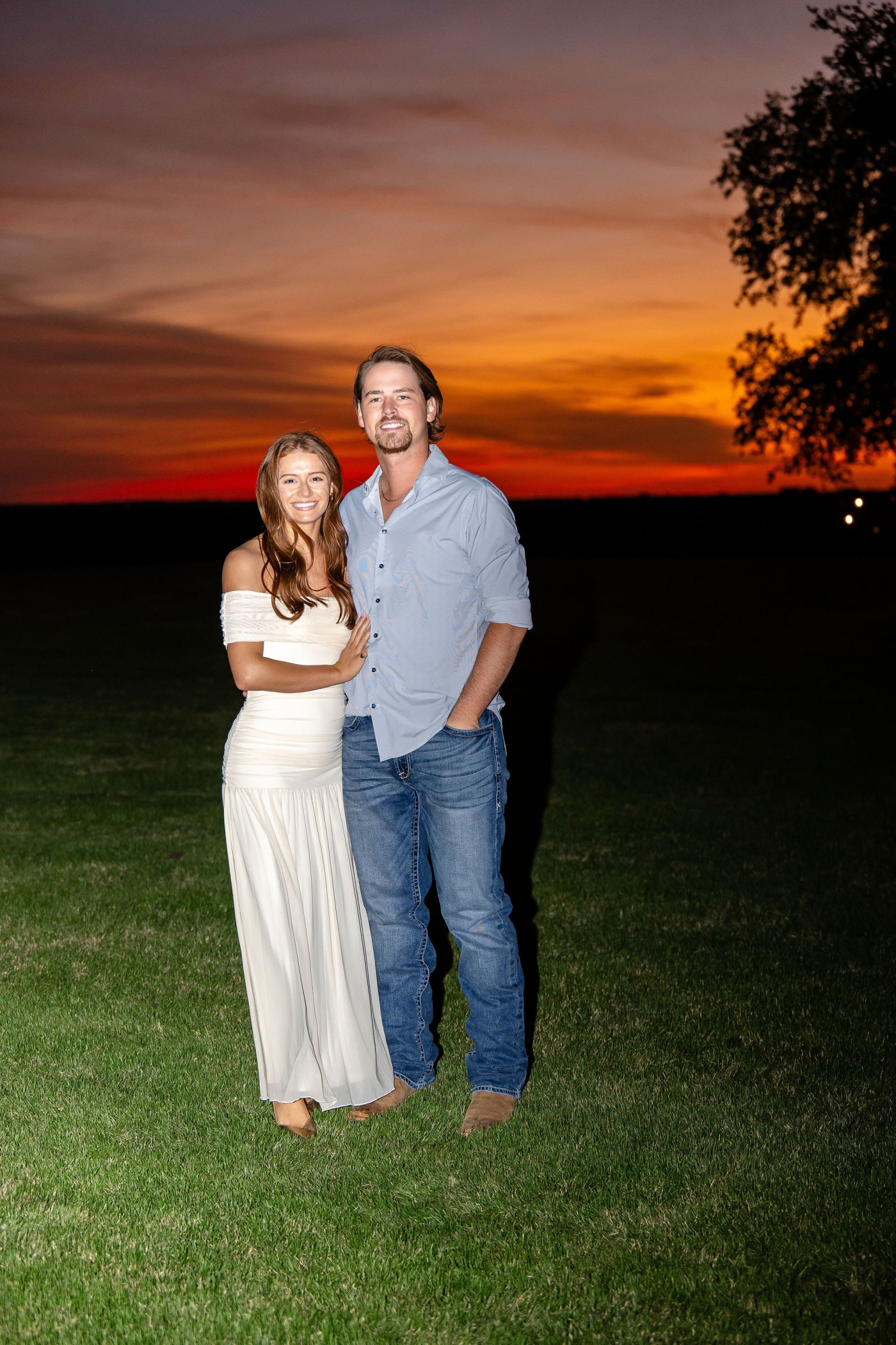 A bride and groom smile as the sun sets behind them in a vivid orange