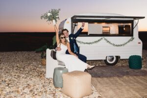 A bride and groom pose in front of a food truck