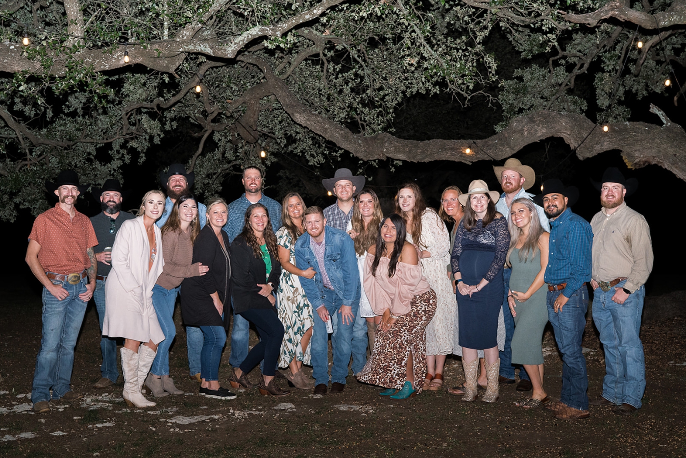 Guests at a wedding weekend are posing beneath the oaks at the Diamond A Ranch