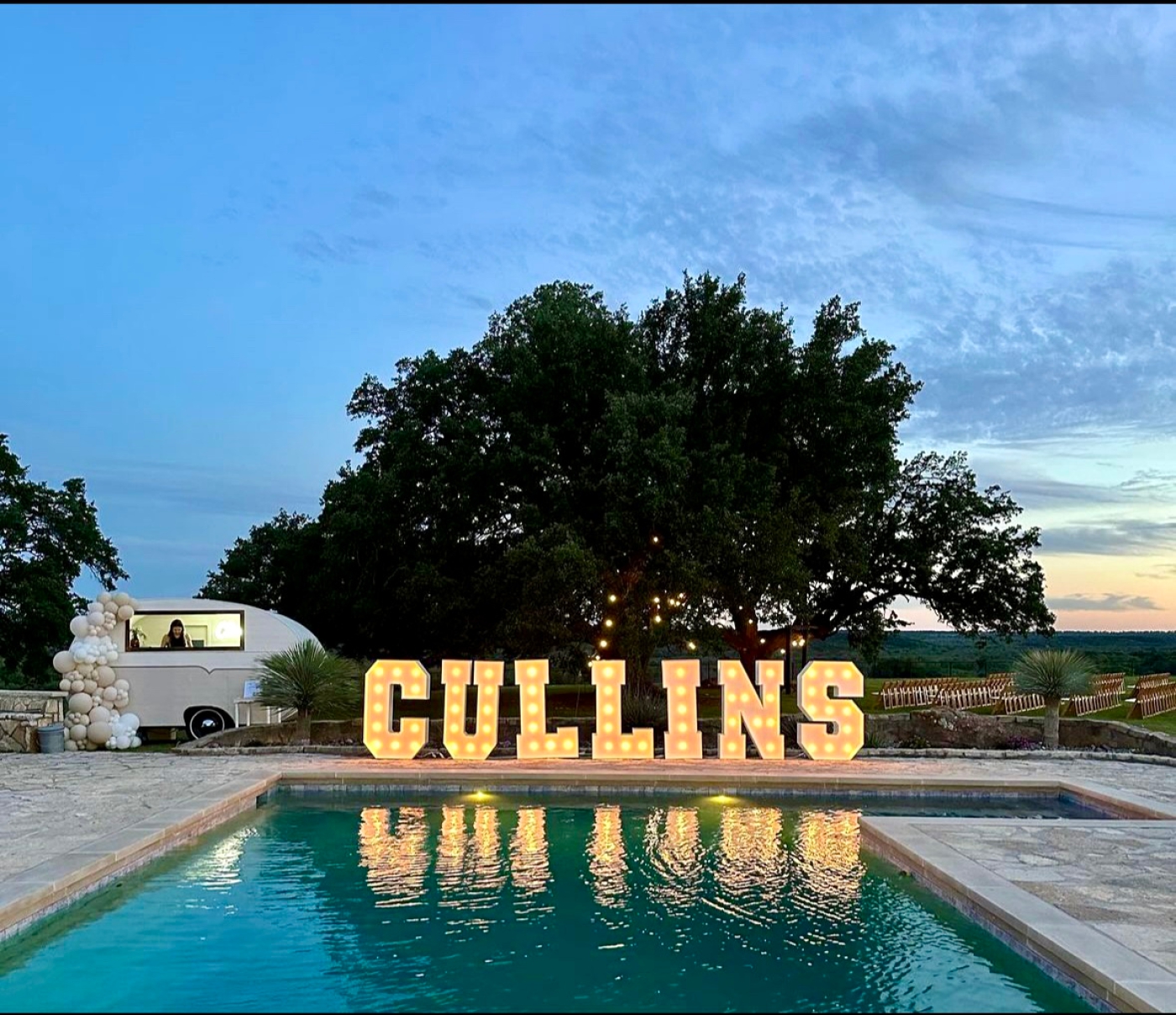 A large light-up sign of a couple's last name stands by a pool