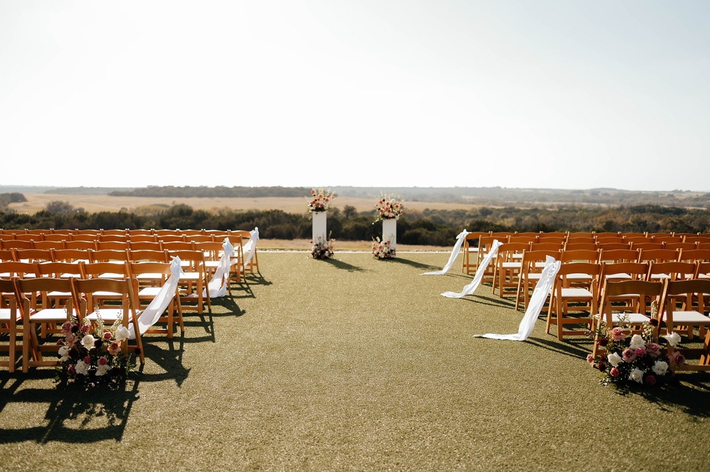 A ceremony set up at a ranch wedding venue with each end char decorated with a white bow