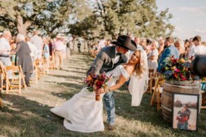 A groom in a cowboy hat dips his bride as they walk up the aisle after their wedding ceremony