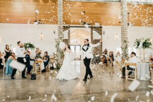 A bride and groom enter their wedding reception beneath a cloud of white confetti